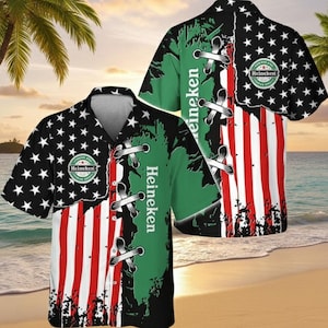 Puede incluir: Camisa de manga corta con un dise&ntilde;o &uacute;nico. La camisa presenta un dise&ntilde;o dividido con la bandera estadounidense en un lado y un dise&ntilde;o verde y negro con la palabra "Heineken" en el otro. El logotipo de Heineken tambi&eacute;n es visible.