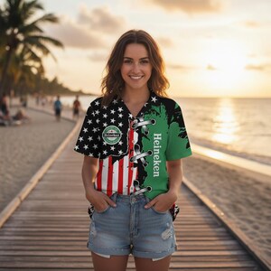 Puede incluir: Una camisa de manga corta con un dise&ntilde;o &uacute;nico. La camisa presenta un dise&ntilde;o dividido con la bandera estadounidense en un lado y un mapa verde con el logotipo de Heineken en el otro. La camisa se usa con pantalones cortos de mezclilla.