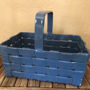 May include: A blue rectangular basket with a handle. The basket has a woven design and is made of a glossy material. The handle is attached to the top of the basket and is also blue.
