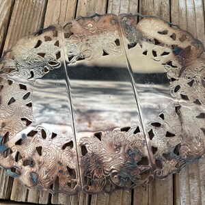 May include: An antique silver-plated serving tray with an ornate floral and scroll design. The tray is divided into three sections and features a scalloped edge with cut-out details. A vintage piece for serving food.