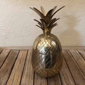 May include: A gold pineapple-shaped ice bucket with a textured surface. The bucket is made of metal and has a lid.