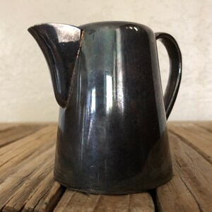 May include: A silver creamer with a rounded body and a curved handle. The creamer has a shiny, reflective surface.