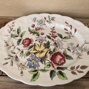 May include: A white oval serving platter with a floral design. The flowers are in shades of pink, yellow, blue, and green. The platter has a scalloped edge.