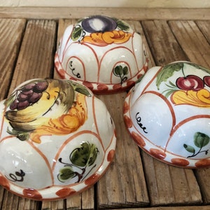 May include: Three white ceramic bowls with a red rim and painted fruit designs. The bowls feature a grape design, a cherry design, and a plum design.