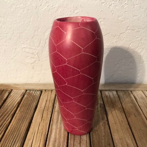 May include: A pink ceramic vase with a white geometric pattern. The vase has a rounded bottom and a narrow opening.