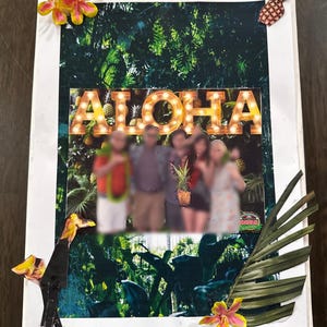 May include: A framed collage with a tropical theme. The word "ALOHA" is spelled out in illuminated letters. The collage includes a blurred photo of people, pineapple imagery, and decorative flowers and leaves.