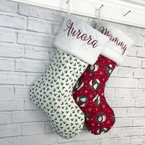 Peut inclure: Deux chaussettes de Noël avec des revers matelassés blancs portant des noms brodés. La chaussette de gauche est en tissu blanc avec un motif de houx vert et rouge. La chaussette de droite est rouge avec des ours polaires et des flocons.