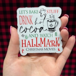 May include: White sticker with red and green text that reads "Let's bake stuff, drink hot cocoa and watch Hallmark Christmas movies". The sticker features a gingerbread man, a cup of hot cocoa with steam, and a Christmas tree.