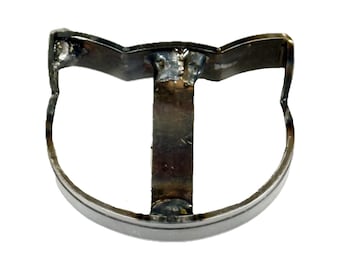 May include: A cat-shaped metal frame constructed from welded steel strips. The object features a curved bottom base, two pointed ears at the top, and a vertical support bar connecting the center of the base to the top edge, showing visible weld marks.