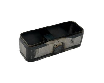 May include: A rectangular metal container with rounded corners, featuring a dark, unfinished steel surface with visible grinding marks and weld spots along the exterior sides. The interior is hollow and dark, showing a raw industrial metal finish.
