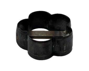 May include: A black metal cookie cutter shaped like a four-petaled flower. The cutter features a continuous, curved outer wall forming the floral silhouette and a straight, horizontal metal bar spanning the center of the open interior space.