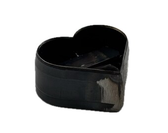 May include: A black heart-shaped metal cutter with a smooth, dark finish and a visible weld seam on the side. The object features a hollow center and a rigid, curved wall structure, showing signs of metallic texture and industrial construction.
