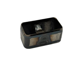 May include: A rectangular metal cutter with rounded corners, featuring a dark, heat-treated finish with visible metallic grinding marks on the exterior sides and a small welded metal tab attached to the inner wall of the hollow frame.