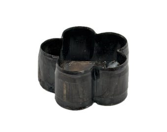 May include: A black, four-lobed flower-shaped cookie cutter with a smooth, continuous metal wall. The object features a hollow center and a uniform dark finish, designed with a rounded, symmetrical outline resembling a simple blossom shape.