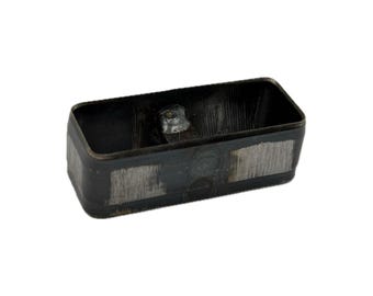 May include: A rectangular metal cutting die with a hollow center and rounded corners. The exterior surface features a dark, oxidized finish with visible brushed metallic patches and a central welded joint on the inner wall.