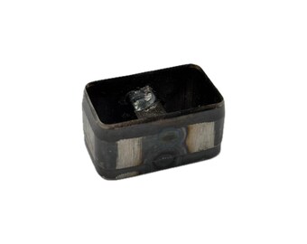 May include: A rectangular metal die cutter with rounded corners, featuring a dark, heat-treated steel finish with visible weld marks and metallic silver sections along the exterior walls and a hollow center.