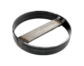 May include: A circular metal ring with a flat horizontal bar welded across the center. The object features a dark, raw steel finish with visible weld marks at the points where the central bar connects to the outer circular frame, creating a sturdy structure.