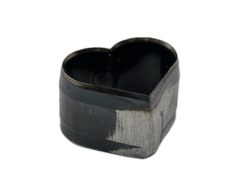 May include: A heart-shaped metal cutting die with a dark, oxidized finish and a sharp, beveled edge. The tool features a hollow center and a sturdy, rigid construction designed for precision cutting tasks, showing visible signs of industrial use.