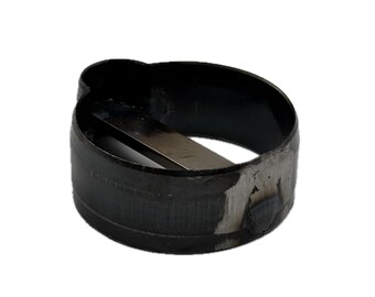 May include: A circular black metal band featuring a protruding tab on one side and a flat, horizontal metal bar spanning the interior diameter. The exterior surface shows signs of wear with visible metallic scuffing and a welded seam.
