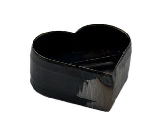 May include: A heart-shaped metal cutting die with a dark, oxidized finish and a sharp, beveled edge. The tool features a continuous, rigid wall forming the heart silhouette, with visible metallic texture and signs of industrial manufacturing.