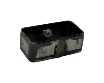 May include: A rectangular metal component with rounded corners, featuring a dark, unfinished steel surface with visible weld marks and grinding textures along the exterior sides and a central interior support bar.
