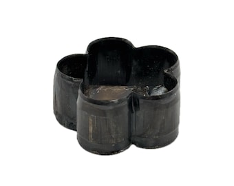 May include: A black, four-lobed flower-shaped cookie cutter made of a rigid material. The object features a continuous, curved wall forming a symmetrical petal design with an open top and bottom, showing a smooth, dark, and reflective surface finish.