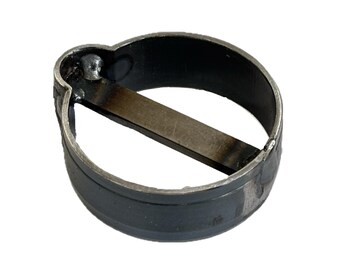 May include: A circular metal band featuring a dark, weathered finish with a straight metal bar welded across the center. The structure includes a small, rounded protrusion on one side where the bar connects to the outer ring, showing visible weld marks.
