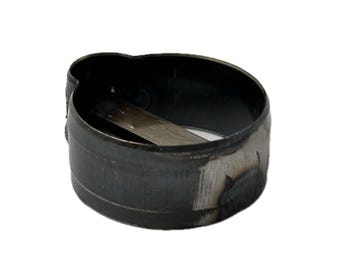 May include: A circular metal clamp with a dark, unfinished steel surface. The band features a distinct protruding hump on one side and a flat, rectangular metal tab extending across the interior diameter of the ring, showing signs of welding.