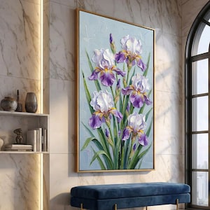 May include: A framed floral painting featuring white and purple iris flowers with yellow accents and green leaves. The artwork is set against a light blue textured background and framed in gold. The painting is displayed in a room with a blue bench.