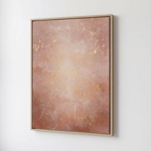 May include: Abstract art print in a wooden frame. The artwork features a blend of peach, pink, and gold tones, creating a soft, textured appearance. The painting has a light center and darker edges.