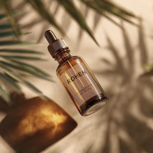May include: A clear glass bottle with a brown liquid and a dropper top. The bottle is labeled with the word "ROHEN". The background features shadows of palm leaves on a beige surface.