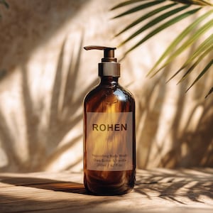 Puede incluir: Una botella de vidrio marrón con dispensador de bomba, etiquetada "ROHEN" y "Nourishing Body Wash." La botella contiene 200 ml de producto. La imagen está sobre una superficie de madera con sombras de una planta.