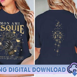 May include: Navy blue t-shirt with gold text and graphics. The front features the words "Mon Ami Esquie" and a rose graphic. The back has a sun and star design with the number "33". The text "Master of Sky, Sea... and Naps" is also visible.