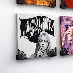 Puede incluir: Impresión artística en lienzo en blanco y negro que presenta a una mujer con cabello largo y el texto "MEDUSA ANGELS". La impresión está montada en una pared blanca con soportes decorativos negros.