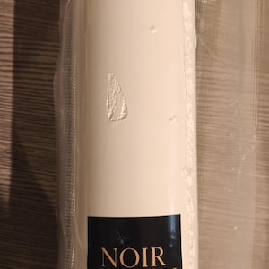 May include: A cylindrical white product, possibly a food item, encased in clear plastic. The product has a label that reads "NOIR STARCH" in a black rectangle. The packaging is sealed, suggesting freshness.