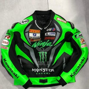 Könnte beinhalten: Schwarze und grüne Kawasaki Motorrad-Rennjacke mit mehreren Sponsorenlogos, darunter Monster Energy und Pirelli. Die Jacke hat ein Ninja-Logo und ist aus Leder.