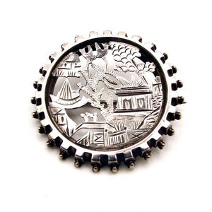 May include: A silver brooch with a circular design featuring a cut-out scene of a Chinese garden with a pagoda, trees, and birds.