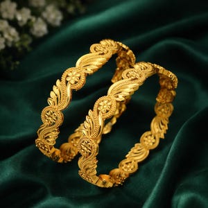 Könnte beinhalten: Zwei goldene Armreifen mit aufwendigen Blumen- und Blattmustern. Die Armreifen bestehen aus glänzendem, gelbem Metall und sind vor einem dunkelgrünen, seidigen Hintergrund platziert. Die floralen Muster sind detailliert und wiederholen sich am Umfang der Armreifen.