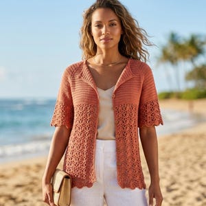 May include: A coral-colored, short-sleeved crochet cardigan with a scalloped hem and button closure. The openwork design adds a delicate touch. The cardigan is paired with white pants and a straw clutch, creating a relaxed, beachy aesthetic.