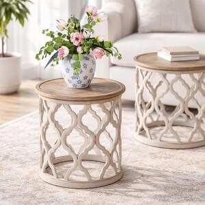 Puede incluir: Dos mesas auxiliares decorativas con tapa de madera clara y base calada color crema. Una mesa sostiene un jarr&oacute;n con flores rosas y vegetaci&oacute;n. Las mesas est&aacute;n sobre una alfombra estampada.
