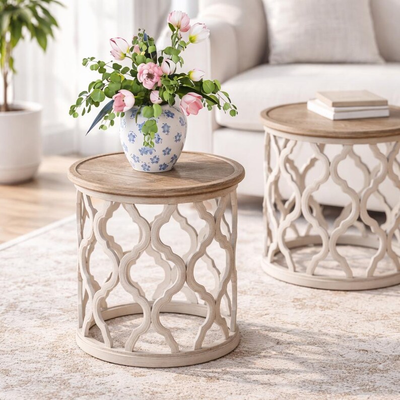 Puede incluir: Dos mesas auxiliares decorativas con tapa de madera clara y base calada color crema. Una mesa sostiene un jarr&oacute;n con flores rosas y vegetaci&oacute;n. Las mesas est&aacute;n sobre una alfombra estampada.