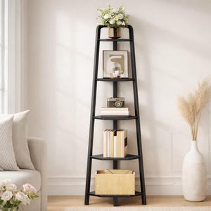 May include: A black corner bookshelf with five shelves, holding decorative items like a framed print, a vintage camera, books, and a wooden box. A vase of flowers sits on top. The bookshelf is placed in a living room setting.