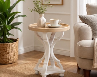 May include: A round side table with a light wood top and a white base featuring curved legs and a small lower shelf. On the table sits a white ribbed ceramic vase containing green leafy stems and a white ceramic cup on a matching saucer.