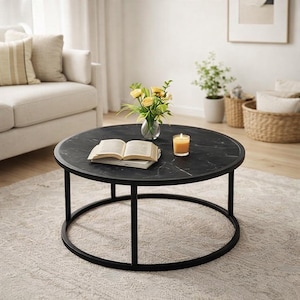 May include: A round black coffee table with a marble-like top and a black metal frame. The table holds an open book, a vase of yellow flowers, and a lit candle. The table is set on a patterned rug.