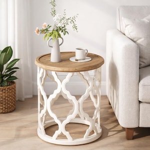 Puede incluir: Una mesa auxiliar redonda con una base blanca con un dise&ntilde;o geom&eacute;trico abierto. La tapa es de color marr&oacute;n claro y tiene un peque&ntilde;o jarr&oacute;n con flores y una taza de caf&eacute;. La mesa est&aacute; junto a un sof&aacute; de color claro.