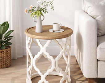 May include: A round side table with a white base featuring an open, geometric design. The tabletop is light brown, and it holds a small vase with flowers and a cup of coffee. The table is next to a light-colored sofa.