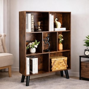 May include: A dark brown wooden bookshelf with multiple cubbyhole shelves. The shelves are filled with books, decorative items, and a woven basket. The bookshelf has black legs and is placed against a neutral wall.