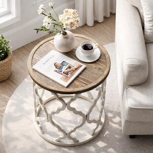 Puede incluir: Una mesa auxiliar redonda de madera con base de metal blanco. La mesa tiene una tapa de color marr&oacute;n claro con un borde decorativo. Un jarr&oacute;n blanco con flores, una taza de caf&eacute; y una revista est&aacute;n sobre la mesa. La revista se titula "KINFOLK".