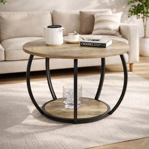 May include: Round coffee table with a light wood top and a black metal frame. The table has a lower shelf and a glass vase with decorative objects. A white teapot, cup, and book are on the table.
