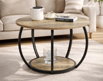 May include: Round coffee table with a light wood top and a black metal frame. The table has a lower shelf and a glass vase with decorative objects. A white teapot, cup, and book are on the table.